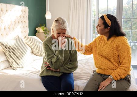 Mère senior et fille assis sur le lit réconfortant avec la main sur l'épaule à côté de la lampe suspendue Banque D'Images