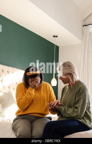 Diverses amies féminines assises sur le lit dans la chambre avec tête de lit touffetée se consolant mutuellement Banque D'Images