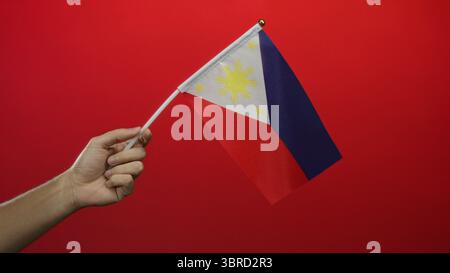 Homme tenant le drapeau philippin sur un fond rouge avec une focalisation isolée mettant en valeur le patriotisme et la fierté nationale. Banque D'Images