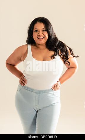 Femme adulte moyenne debout dans le studio les mains sur les hanches portant un débardeur blanc et un Jean denim Banque D'Images