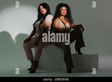 Divers modèles féminins posant dos à dos sur des risers blancs en studio avec bretelles, talons hauts Banque D'Images