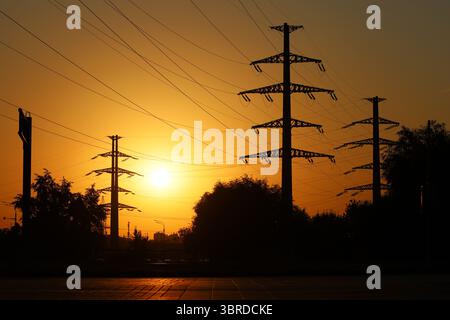Silhouettes de tours haute tension avec des fils électriques sur fond de ciel de coucher de soleil. Lignes de transmission d'électricité en ville, concept d'alimentation électrique Banque D'Images