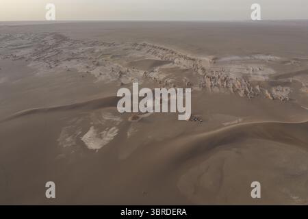 Vue aérienne du paysage désertique sombre et ensoleillé avec des formations sculptées par le vent s'étendant à l'horizon, une symphonie de teintes beige et brune sous un ciel pâle., Kerman, province de Kerman, Iran. Banque D'Images