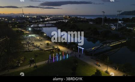 Vue aérienne d'une rivière tranquille reflétant les lumières de la ville, avec des gens se promenant le long de pou rama, sentiers illuminés au crépuscule, Nelson, région de Nelson, Nouvelle-Zélande. Banque D'Images