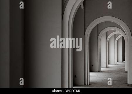 Image monochromatique d'un long couloir avec des arches répétées créant un jeu dramatique de lumière et d'ombre. Une perspective architecturale abstraite. Banque D'Images