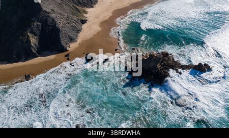 Vue aérienne des falaises accidentées rencontre l'océan turquoise, créant un contraste spectaculaire avec le sable doré de Praia da Cordoama, Algarve, Portugal. Banque D'Images