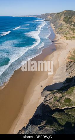 Vue aérienne de la plage dorée de Praia da Cordoama, embrassée par des vagues de saphir et encadrée par des falaises escarpées sous un ciel serein, Praia da Cordoama, Algarve, Portugal. Banque D'Images