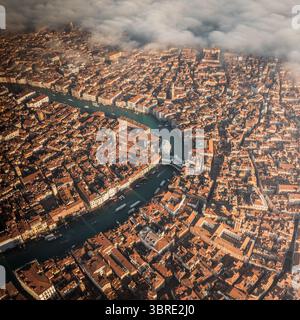 Vue aérienne des toits en terre cuite descendant jusqu'au Grand canal sinueux, où les bateaux glissent sous l'emblématique pont du Rialto, Venise, Vénétie, Italie. Banque D'Images
