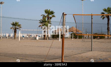 Terrain de Beach volley avec plusieurs filets installés sur du sable, encadré par de grands palmiers et des parasols en paille. La scène capture une atmosphère estivale idéale f Banque D'Images