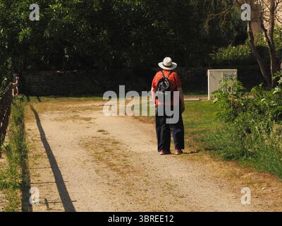 Femme plus âgée portant un chapeau, un chemisier, un pantalon large et un sac à dos sur une voie Banque D'Images