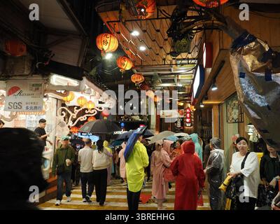 Jiufen, Taiwan - 8 novembre 2024 - les touristes en tenue de pluie et avec des parapluies marchent dans les allées mouillées éclairées par des lanternes de la vieille rue Jiufen la nuit. Banque D'Images