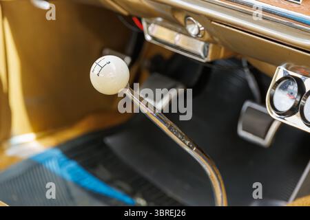 Gros plan du levier de vitesses manuel d'une voiture ancienne avec bouton blanc, bâton chromé et pédalier, mettant en valeur le design automobile classique dans un éclairage chaleureux. Banque D'Images