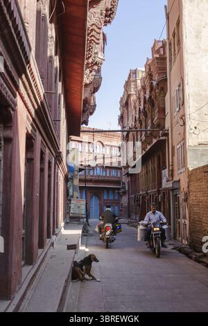 Bikaner, Inde - 24 juin 2025 : vue sur une rue étroite baignée par la lueur chaude du soleil, encadrée par des bâtiments en grès rouge vieilli et la vie quotidienne qui se déroule. Banque D'Images