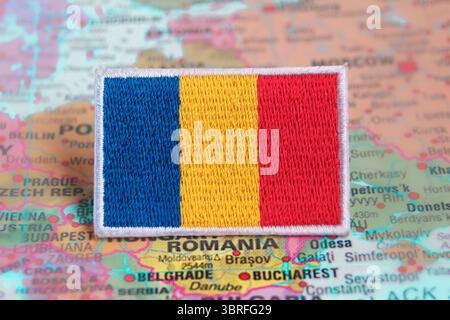Drapeau de Roumanie respectueux de l'environnement brodé à partir de tissu, placé sur l'Europe sur la carte du monde, soulignant l'emplacement du pays et l'identité verte. Banque D'Images
