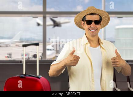 Homme en vacances portant des lunettes de soleil chapeau de chemise jaune à l'aéroport faisant des pouces heureux vers le haut geste avec les mains. Expression d'approbation regardant la caméra wi Banque D'Images