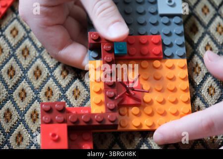 Mains assemblant soigneusement une structure Lego vibrante sur une surface à motifs. Banque D'Images