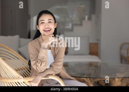 Femme heureuse se relaxant dans une chaise en osier moderne dans le salon Banque D'Images