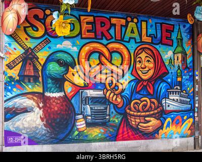 Sodertalje, Suède - 6 juin 2025 : une murale vibrante représentant une femme souriante en tenue traditionnelle tenant un panier de bretzels, aux côtés d'un coloré Banque D'Images