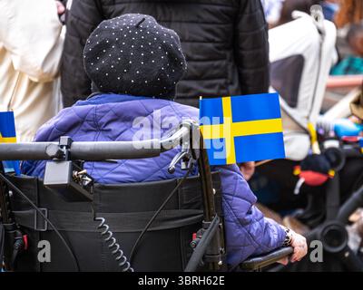 Sodertalje, Suède - 6 juin 2025 : une personne âgée en fauteuil roulant, portant un chapeau à pois, avec un petit drapeau suédois attaché à la chaise. Le BA Banque D'Images