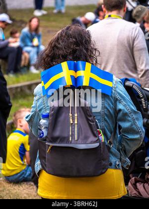 Sodertalje, Suède - 6 juin 2025 : une personne avec un sac à dos orné de drapeaux suédois, assise dans une foule. La scène capture une atmosphère festive, l Banque D'Images
