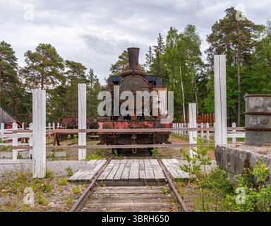 Sodertalje, Suède - 6 juin 2025 : une vieille locomotive à vapeur se dresse sur une voie ferrée désaffectée entourée d'arbres et de poteaux en bois. Le train était le F. Banque D'Images