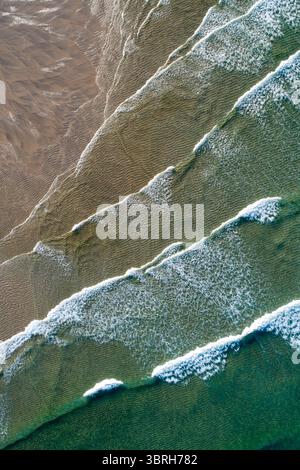 vue aérienne de haut en bas des puissantes vagues de l'océan se brisant sur une plage de sable Banque D'Images