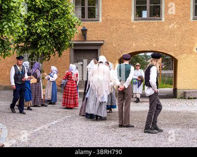 Sodertalje, Suède - 6 juin 2025 : un groupe de personnes vêtues de costumes historiques traditionnels, rassemblées dans une cour. Certains sont engagés dans la conversa Banque D'Images