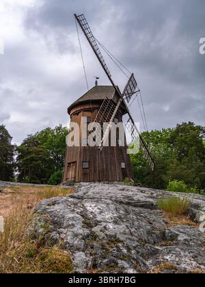 Sodertalje, Suède - 6 juin 2025 : un moulin à vent en bois à Sodertalje se dresse sur un terrain rocheux sous un ciel nuageux, entouré de verdure. Le moulin à vent fe Banque D'Images