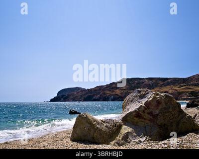 Plage ensoleillée avec de grands rochers éparpillés sur le rivage sablonneux sous un ciel bleu sans nuages. Voyage d'été tranquille ou concept d'évasion dans la nature. Banque D'Images