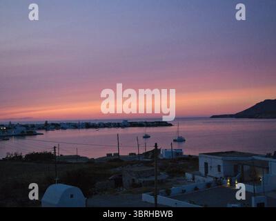 Coucher de soleil sur la baie de Pollonia, île de Milos, avec de petits voiliers sur l'eau calme sous un ciel rose doux. Un paysage marin grec paisible. Banque D'Images