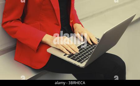 Femme d'affaires travaillant avec un ordinateur portable dans la ville portant une veste blazer rouge, gros plan sur les mains de la femme tapant du texte sur le clavier de l'ordinateur pc Banque D'Images