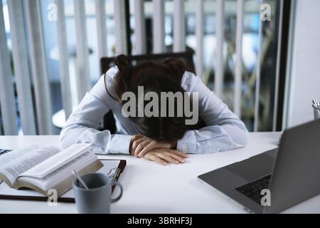 Seul travaillant tard. Femme d'affaires asiatique sur le lieu de travail dans le bureau a couché sa tête sur la table s'est endormie devant l'ordinateur portable Banque D'Images