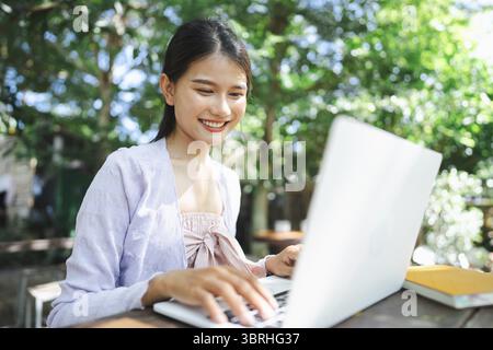 Belle jeune femme asiatique indépendante confiante travaillant avec des mains d'ordinateur portable tapant le clavier. Nomade numérique travaillant à distance à partir de l'éco café extérieur Workp Banque D'Images