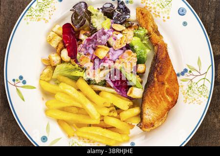 Vue de dessus gros plan de délicieux steak de saumon maison avec salade césar et frits dans une plaque de céramique blanche sur une table en bois Banque D'Images