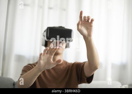 Jeune joueur d'homme asiatique portant la réalité virtuelle touchant l'air pendant l'expérience VR future Home Technology Player hobby concept de plaisir ludique Banque D'Images
