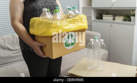 Accueil recycler ECO vert zéro concept Femme jetant bouteille en plastique vide dans le bac de recyclage avec sacs à ordures jaunes à la maison Banque D'Images