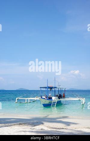 Un bateau traditionnel philippin ou bangka, est amarré sur les eaux turquoises claires d'une plage tropicale paisible et sereine en été Banque D'Images