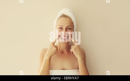 Portrait de femme d'âge moyen caucasienne souriante heureuse pointe vers ses dents blanches propres tout en séchant ses cheveux mouillés avec une serviette enveloppée sur sa tête après s. Banque D'Images