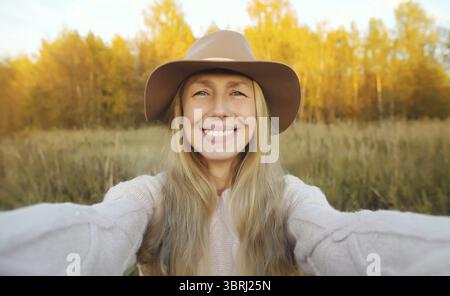 Gros plan portrait de femme mature souriante heureuse prenant selfie avec smartphone dans le parc d'automne, modèle féminin joyeux dans le chapeau à l'extérieur, saison d'automne Banque D'Images