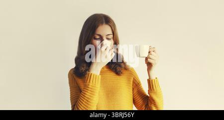 Portrait de femme malade bouleversée éternuant nez de soufflage à l'aide de mouchoir et tenant une tasse de café chaud ou de boisson Banque D'Images