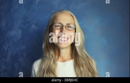 Portrait d'une femme d'âge moyen souriante heureuse dans des lunettes regarde la caméra. Femme blonde senior dans Casual sur fond bleu Banque D'Images