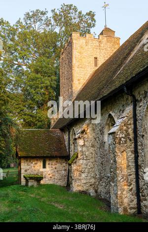 Église St Augustin à Snave dans le Kent. Tôt le matin Golden hour vue le long des murs extérieurs de la nef avec le porche d'entrée et la tour. Banque D'Images