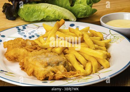 Vue imprenable sur de délicieux poissons cuits faits maison et frits français dans un plat en céramique blanche avec une tasse de sauce maison et légumes verts frais sur le wo Banque D'Images