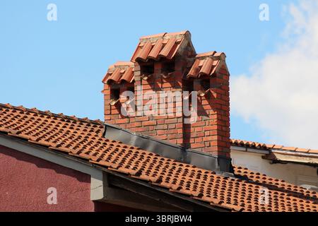 Une cheminée en brique robuste avec trois chapeaux en tuiles de terre cuite s'élève au-dessus d'un toit en tuiles d'argile rouge, mettant en valeur le style architectural méditerranéen classique contre Banque D'Images