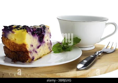 Gros plan vue tranche de gâteau aux myrtilles au yogourt dans un plat en céramique blanche avec une tasse de café et une fourchette en métal isolé sur fond blanc avec chemin de découpage Banque D'Images