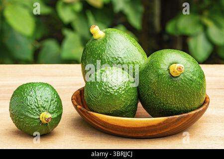 Gros plan vue groupe d'avocats verts frais avec tige dans une plaque en bois sur une table en bois Banque D'Images