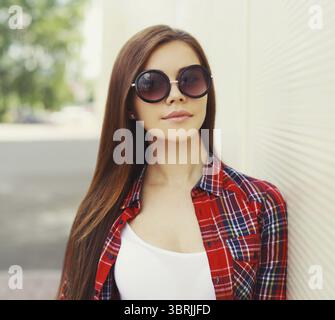 Portrait de belle jeune femme brune portant des lunettes de soleil dans une ville sur fond blanc Banque D'Images