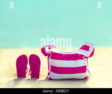 Concept de vacances d'été - sac rose avec tongs sur la plage sur fond bleu de mer Banque D'Images