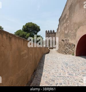 Chemin de pierre à l'intérieur du château de Gibralfaro, menant entre les murs de la forteresse antique sous le soleil avec des arbres et des aperçus de la mer en arrière-plan Banque D'Images