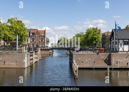 Le pittoresque canal de Lingehaven à Gorinchem, aux pays-Bas, avec ses portes historiques, ses maisons traditionnelles et ses ponts sous un ciel bleu. Banque D'Images